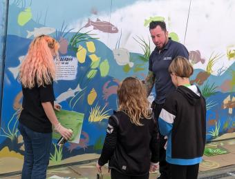A member of The Deep Crew speaking with a group of children at the wall mural.