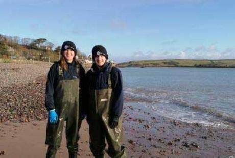 2 people stood on a beach in waders