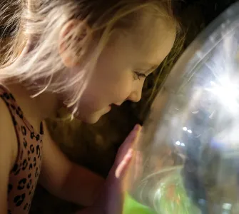 A young girl smiling and looking into one of The Deep's exhibits, with her hand pressed up against the glass.