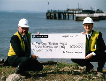 Neil Porteus and David Gemmell crouched for a photo with a cheque for The Deep Millennium Project
