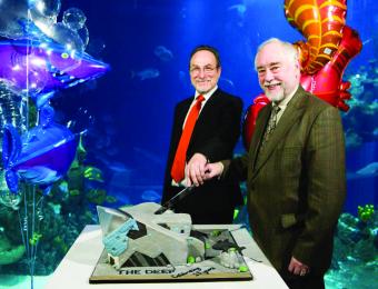 David Gemmell with former Deep CEO Colin Brown, stood cutting a cake shaped like The Deep building.